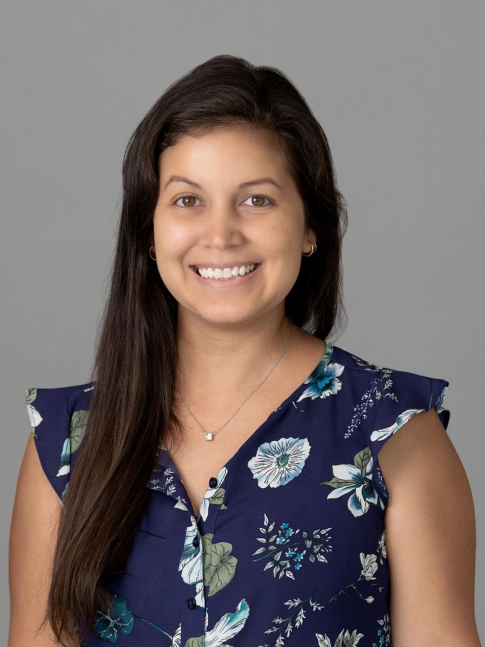 Photo of a woman, Dr. Diana Melo, with long dark hair wearing a floral shirt smiling at the camera.
