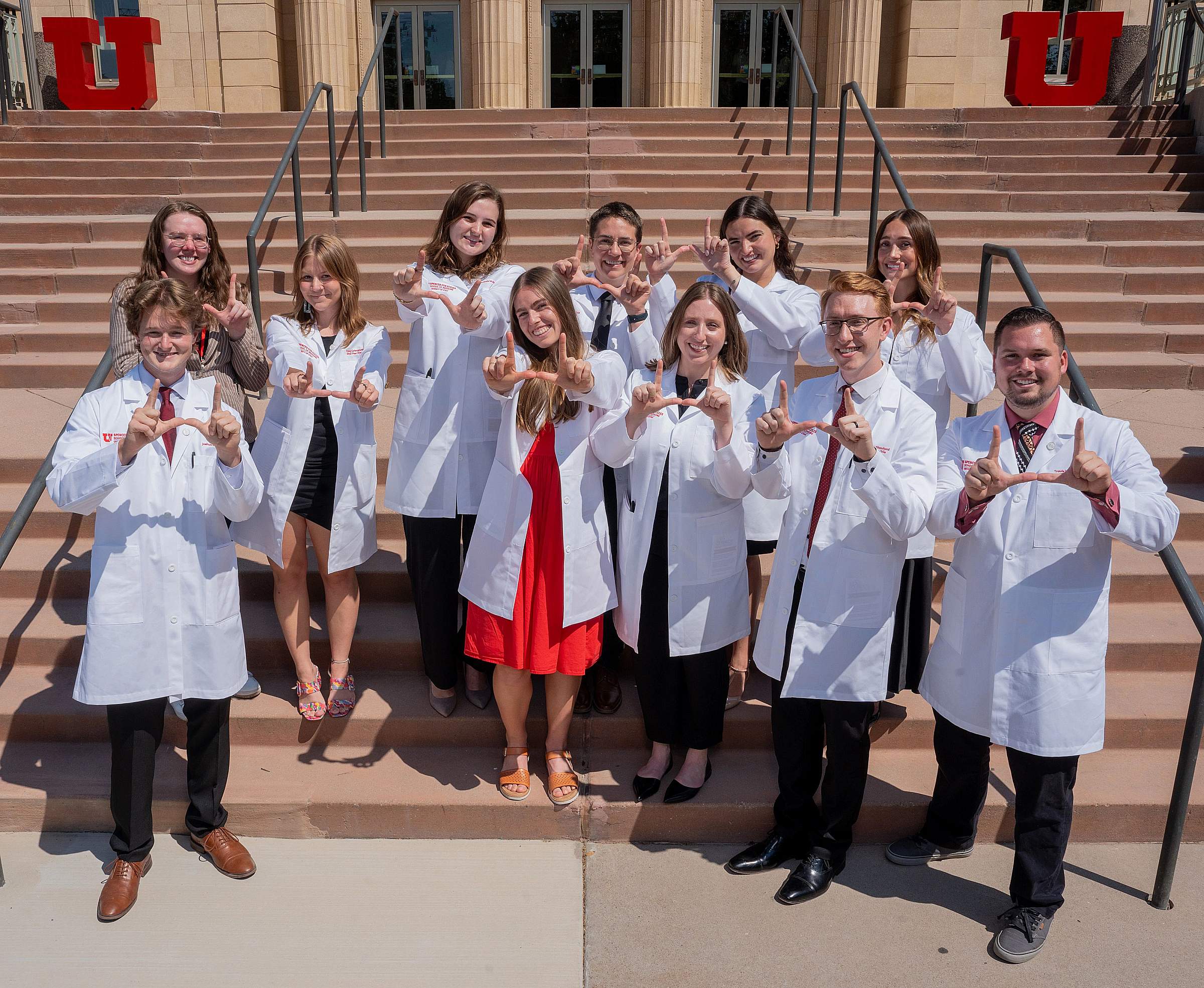 students in white coats flash the U sign 