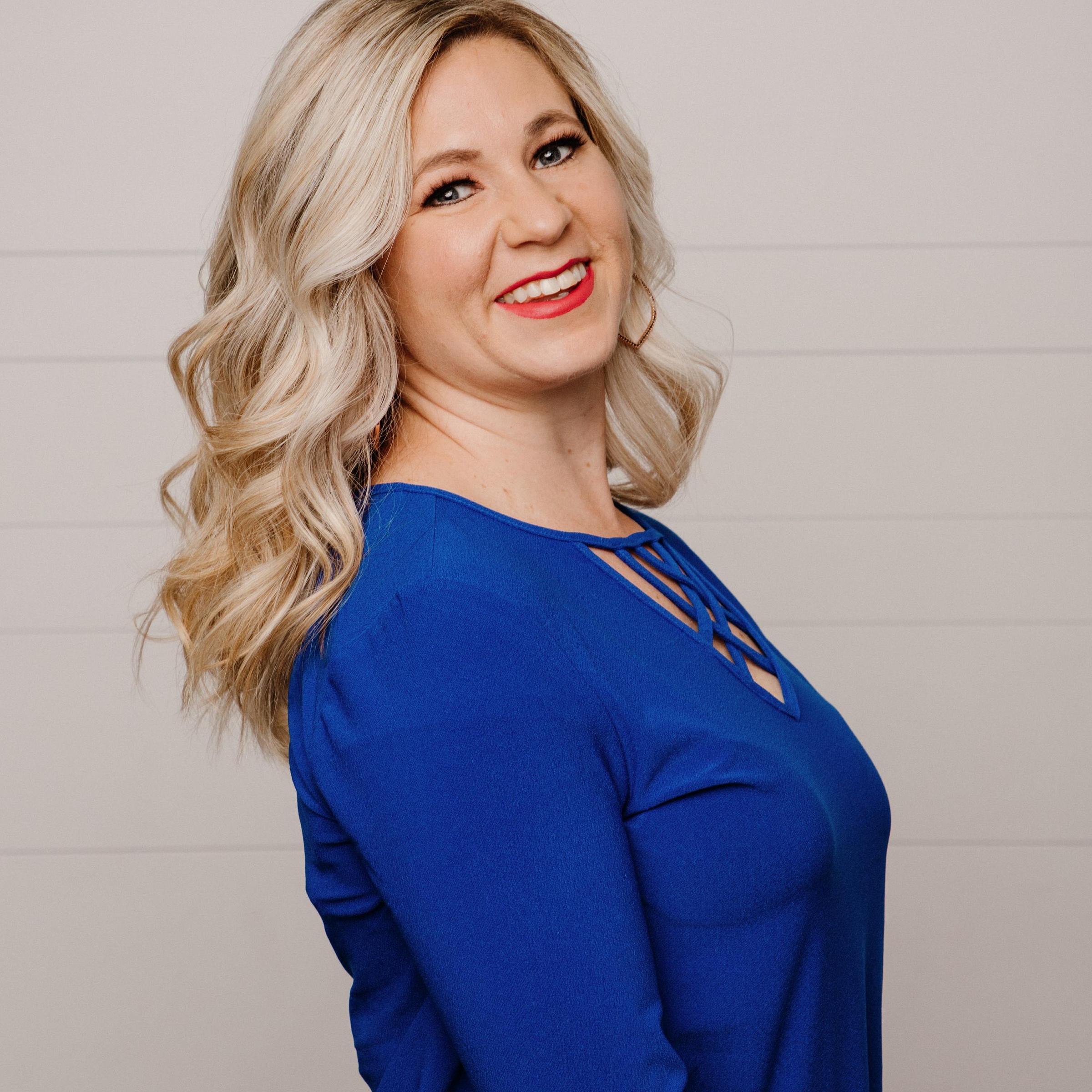 Ashley Hone headshot, long blond curled hair with blue sweater