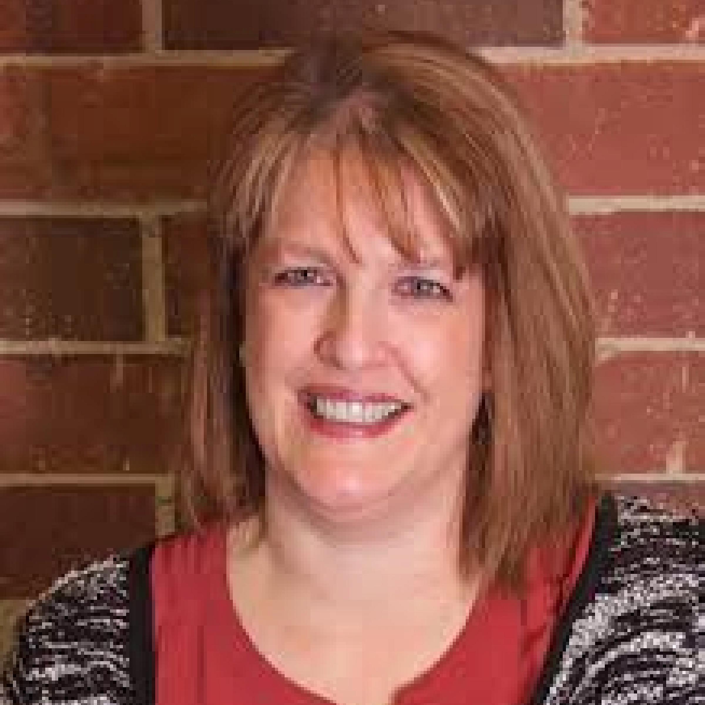 Laurie Baksh smiling headshot with red hair and straight across bangs