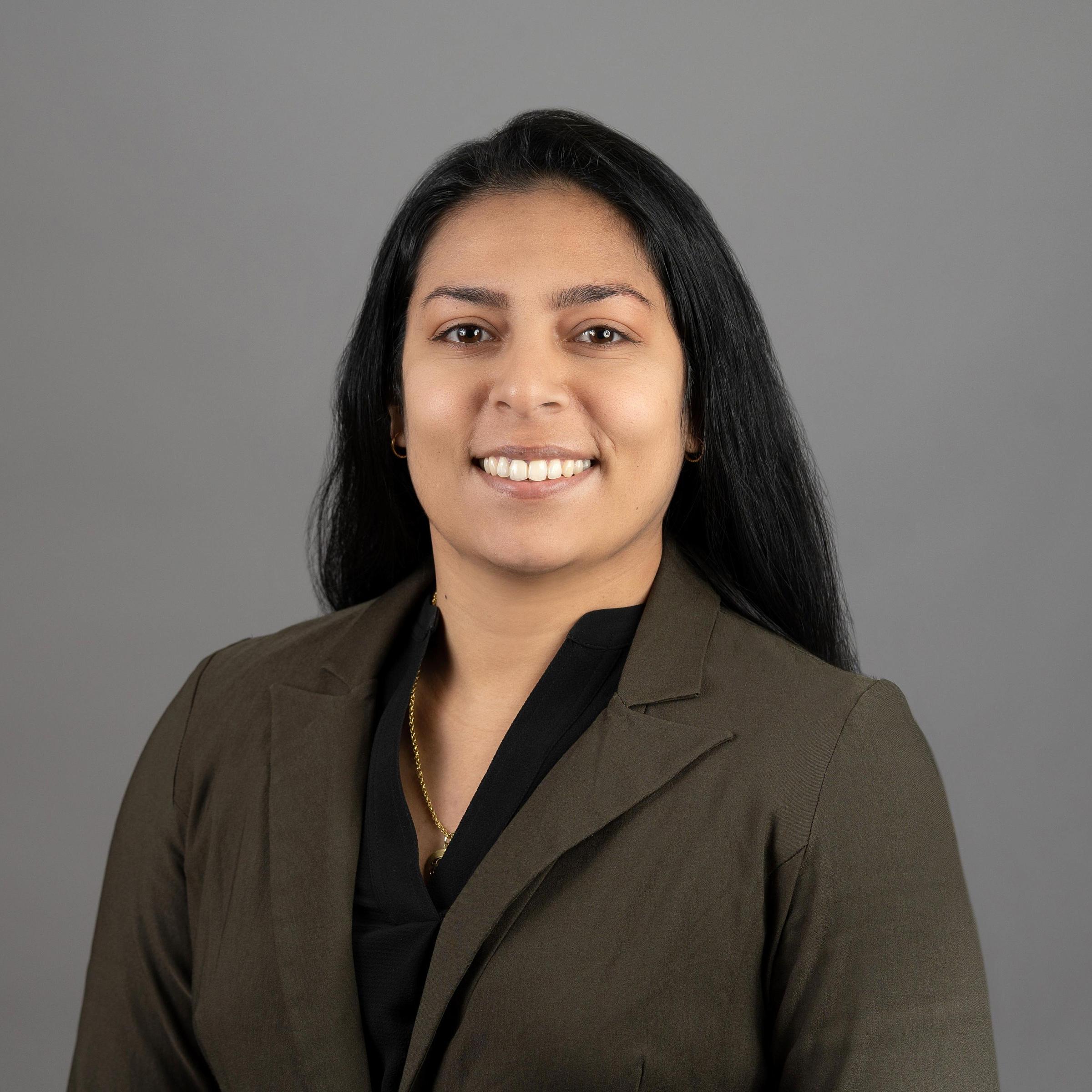 Sunayna Wahi headshot, long dark hair with brown blazer