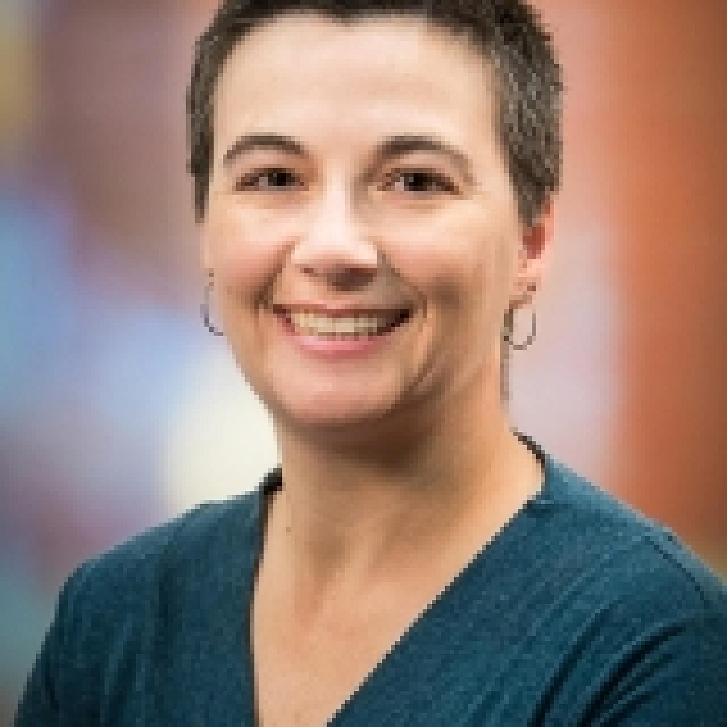 Jessica Comstock smiling headshot with short hair in a blue v neck top