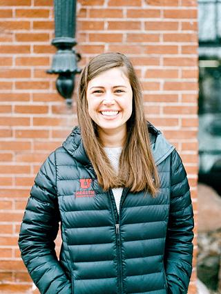 woman with long brown hair standing in front of a red brick wall with a black University of Utah Health Jacket