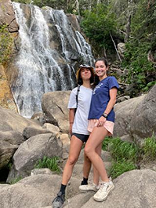 two women standing in front a waterfall