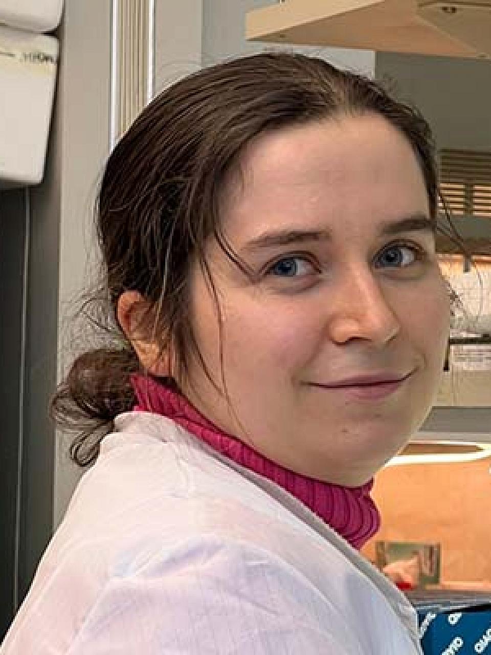 woman with a dark brown hair in a bun, a lab coat and a pink turtleneck