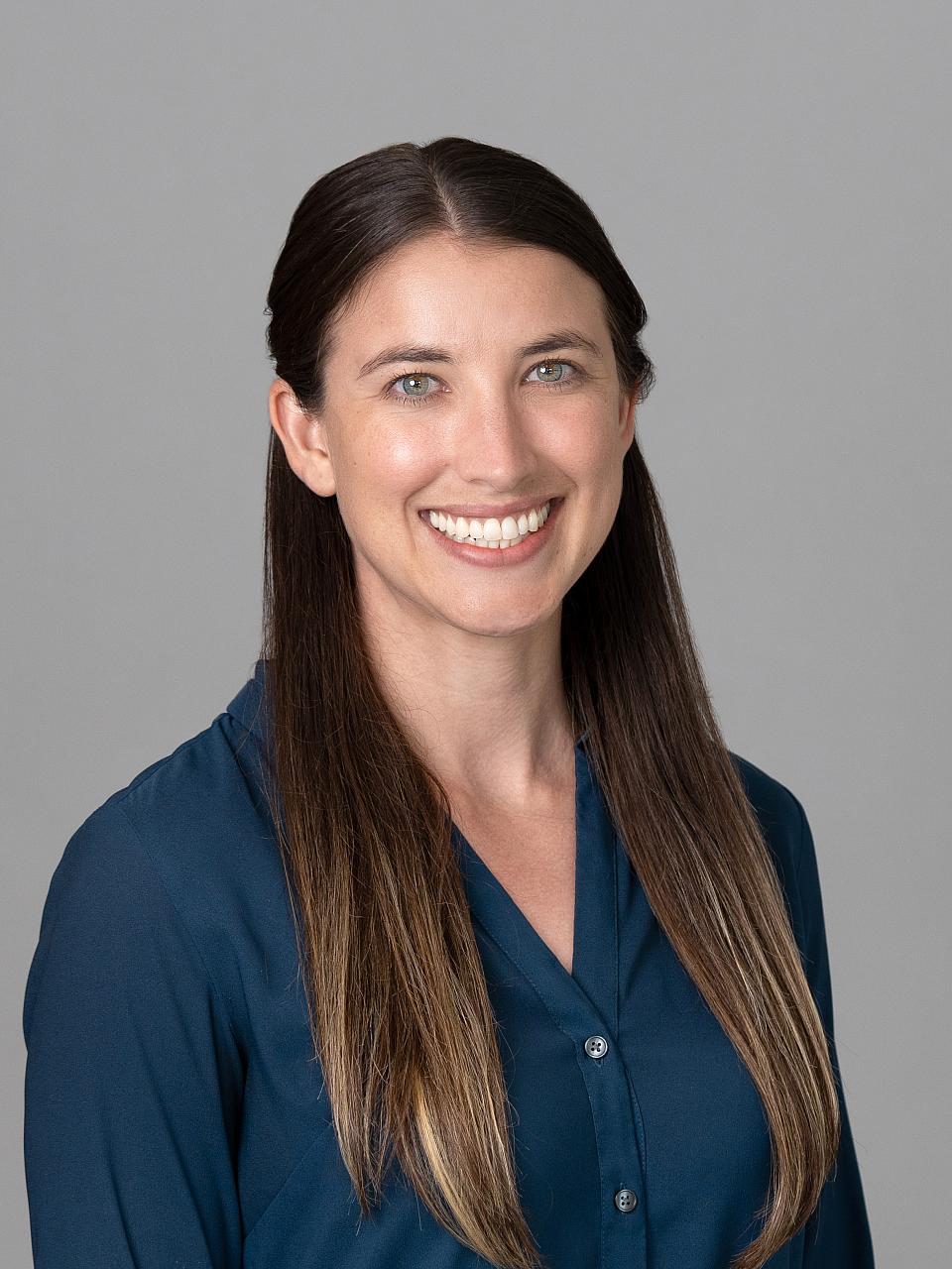 Photo of a woman, Dr. Ashley Goodwin, with long dark hair wearing a dark blue shirt smiling at the camera.