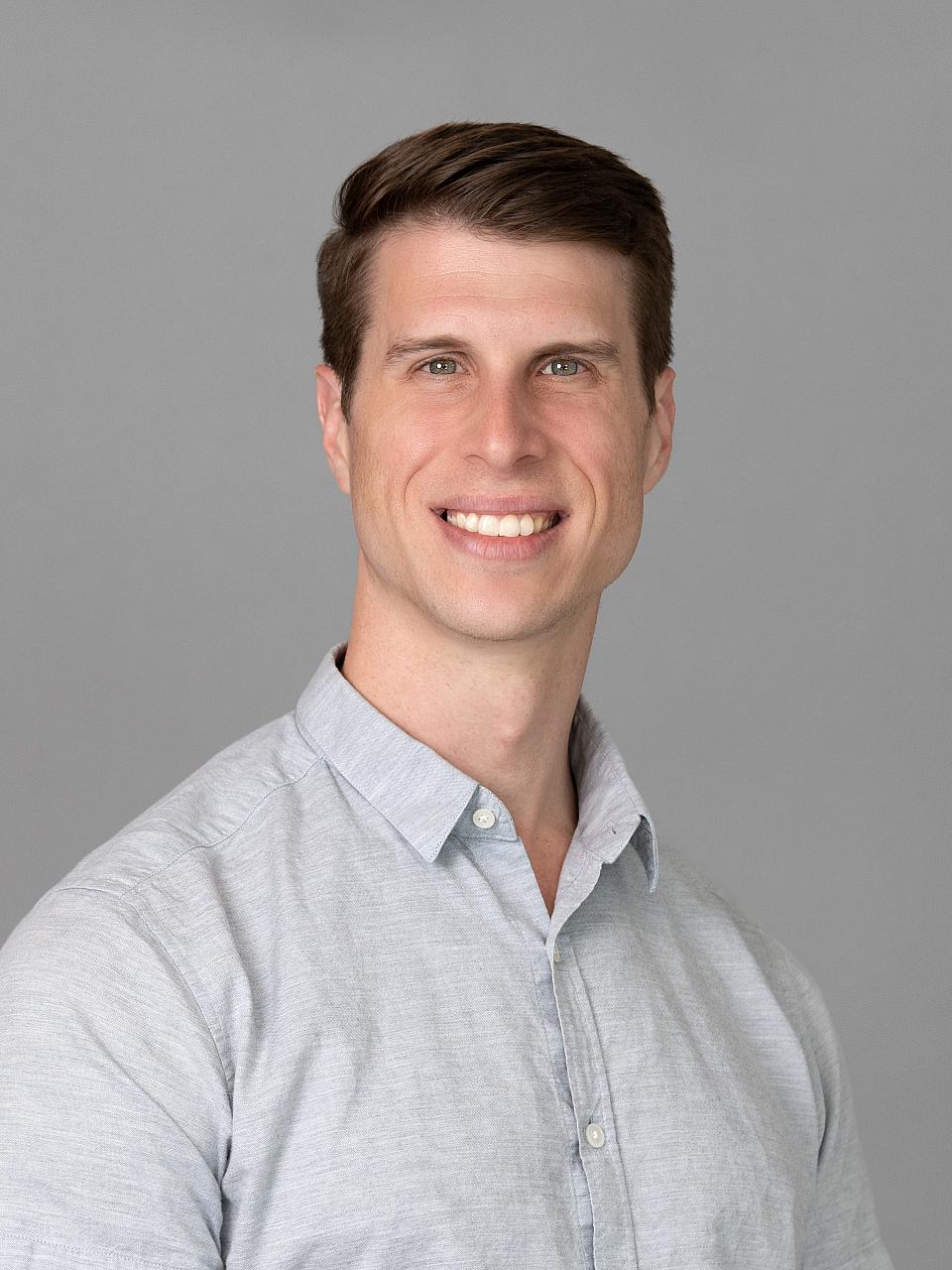 Photo of a man, Dr. Christian Klein, with short dark hair and a light gray shirt smiling at the camera.