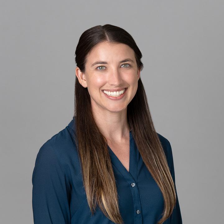 Photo of a woman, Dr. Ashley Goodwin, with long dark hair wearing a dark blue shirt smiling at the camera.
