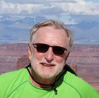 older man with gray hair standing in a lime green shirt and sun glasses. Man is standing in front of red rocks