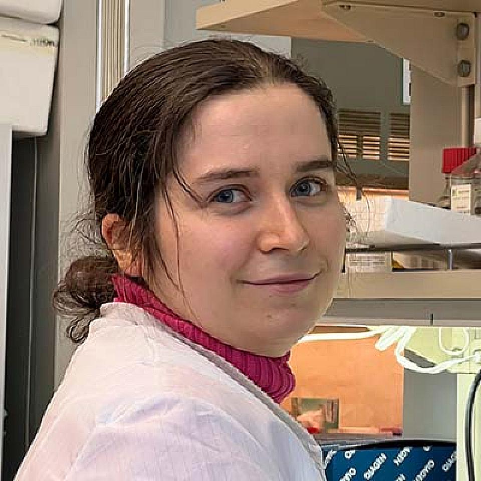 woman with a dark brown hair in a bun, a lab coat and a pink turtleneck