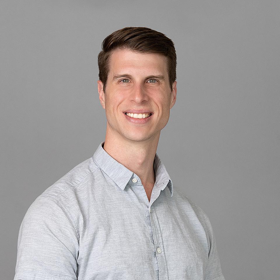 Photo of a man, Dr. Christian Klein, with short dark hair and a light gray shirt smiling at the camera.