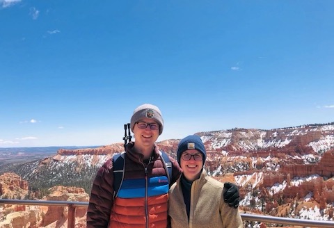 Two people posed in front of a scenic view with a blue sky.