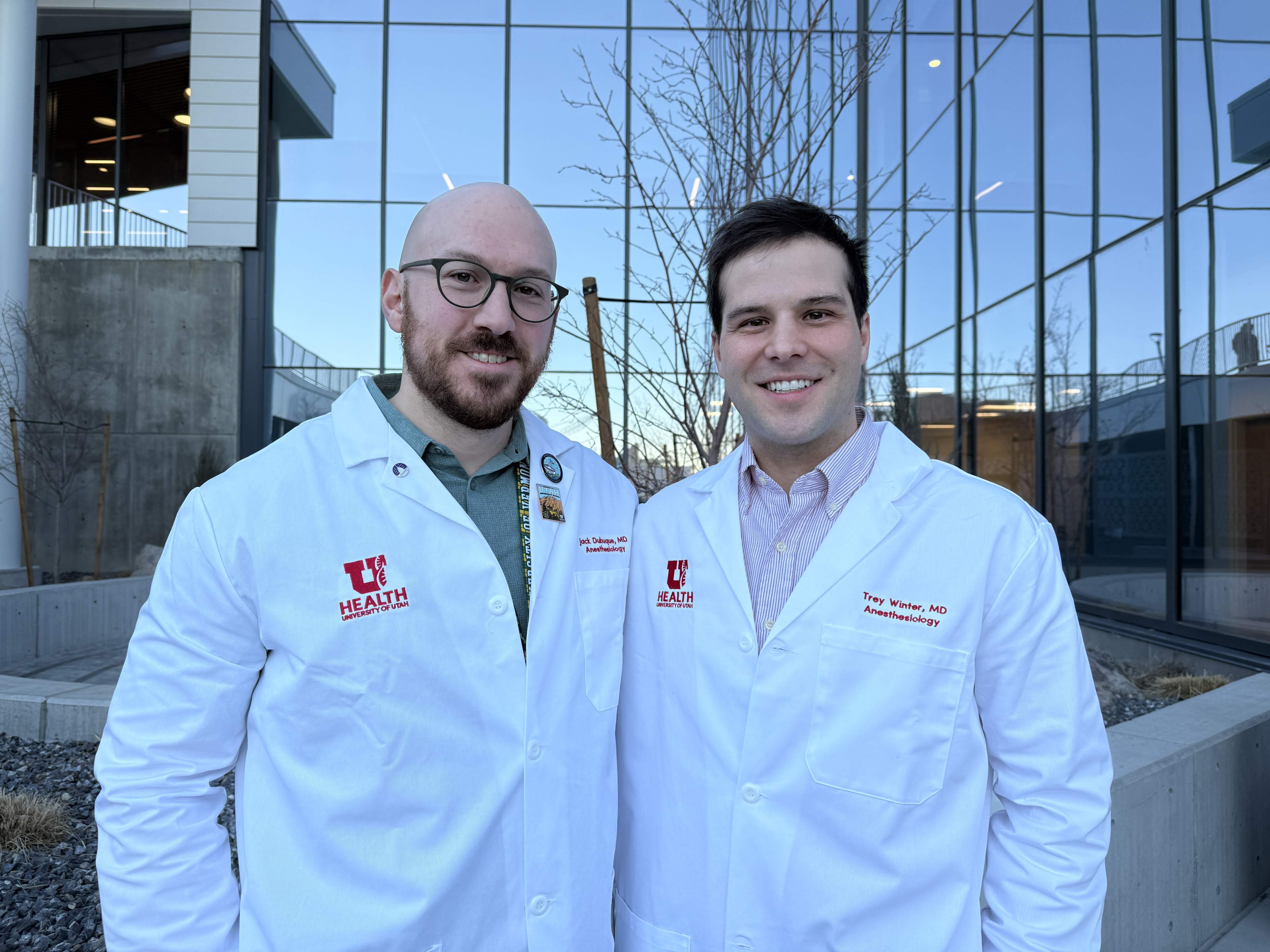 Dr. Jack Dubuque and Dr. Trey Winter standing outside together for a photo after their senior resident presentation. They are wearing their white coats. 