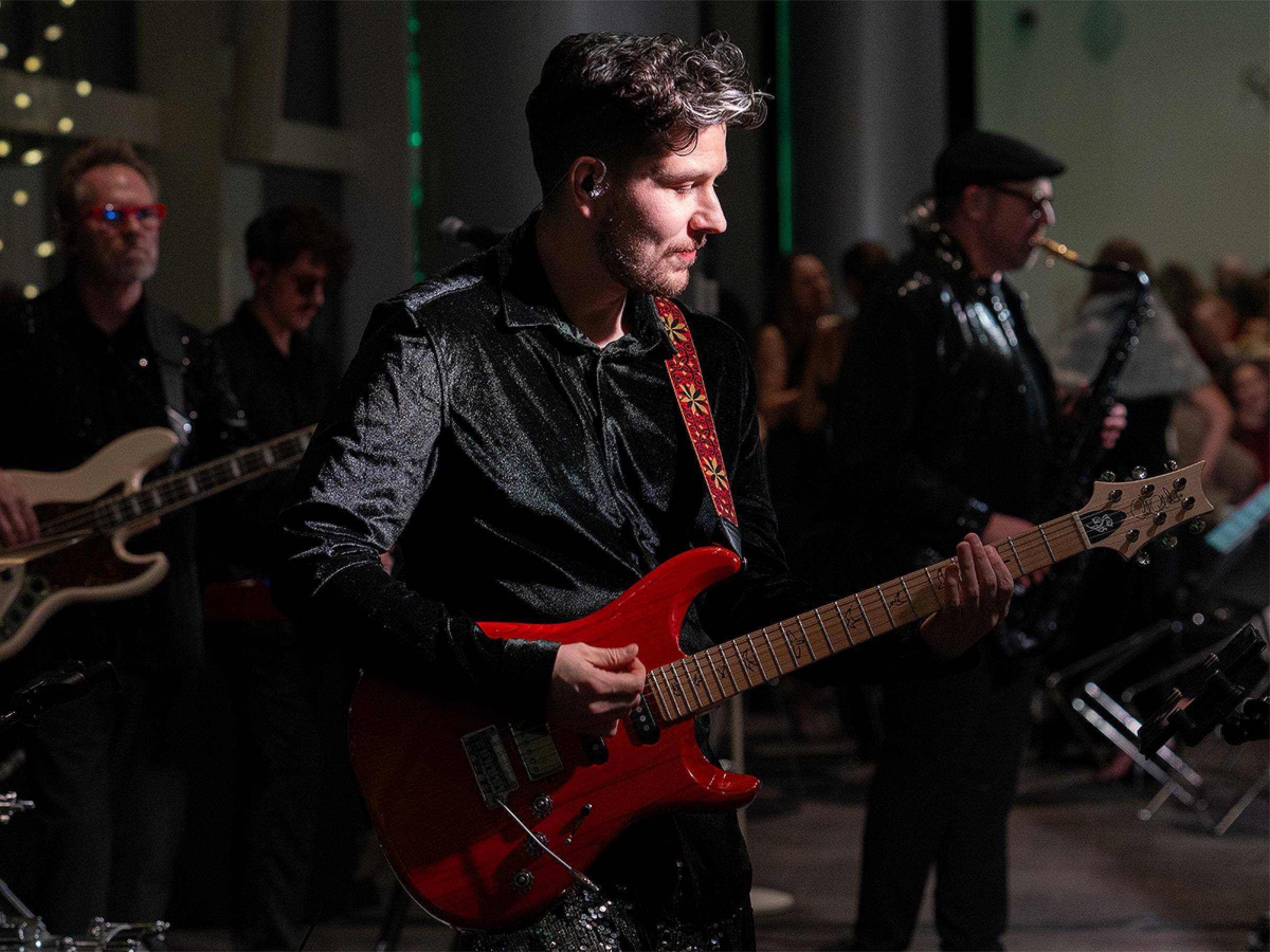 A person playing a red guitar in a sparkly suit. 