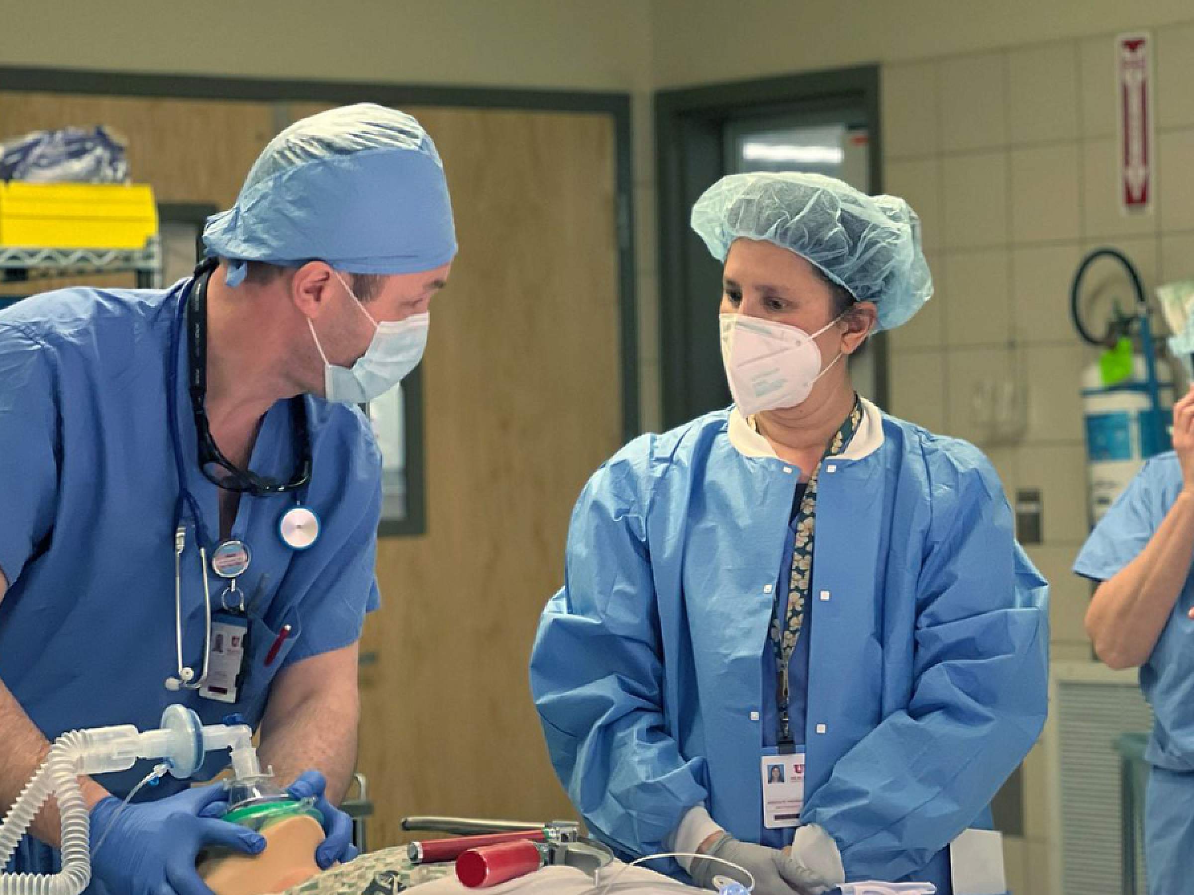Two anesthesiologists in an OR practicing on a mannequin. 