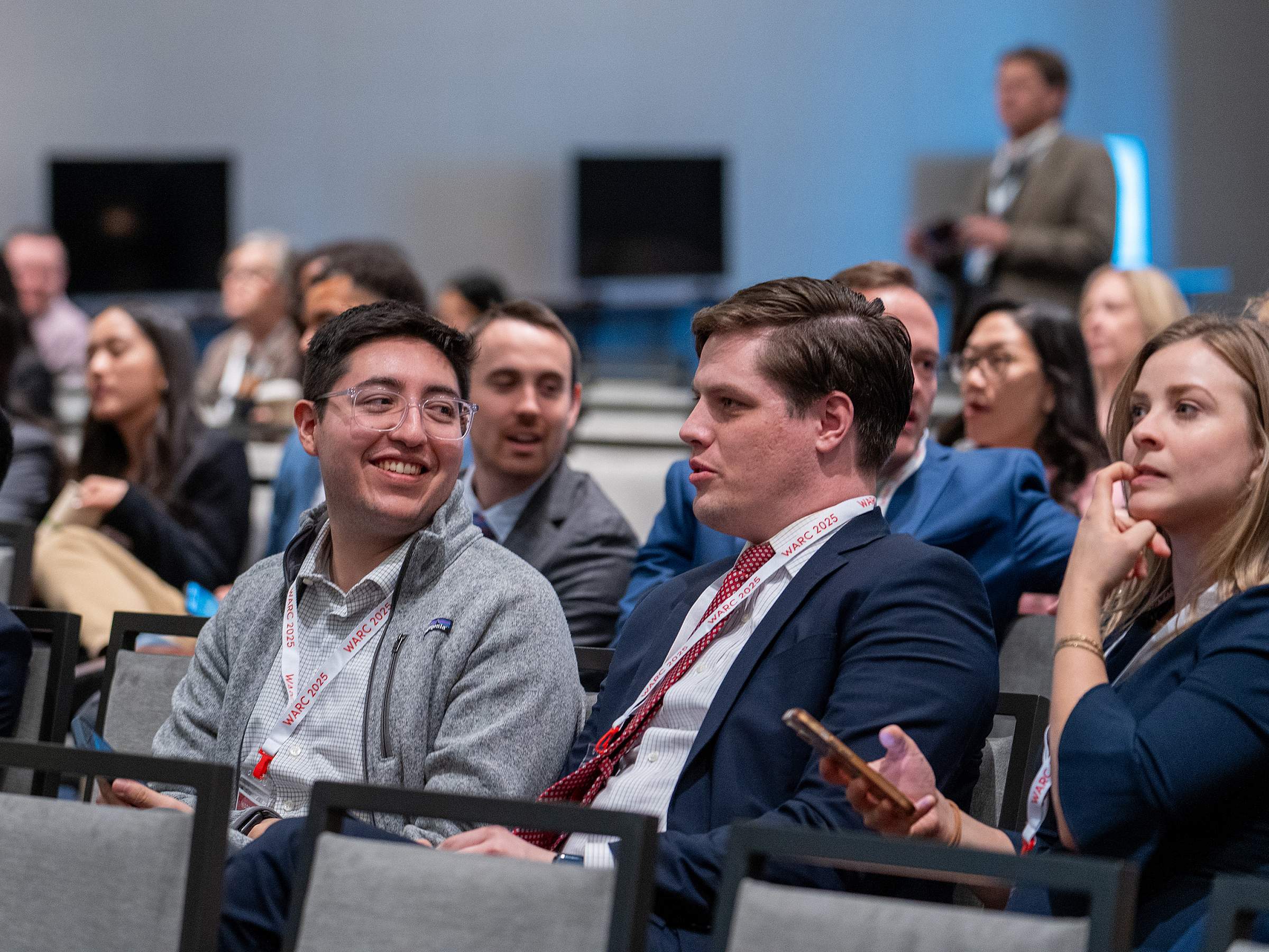 Residents gather in an oral presentation hall, seated in rows and dressed in businesswear.