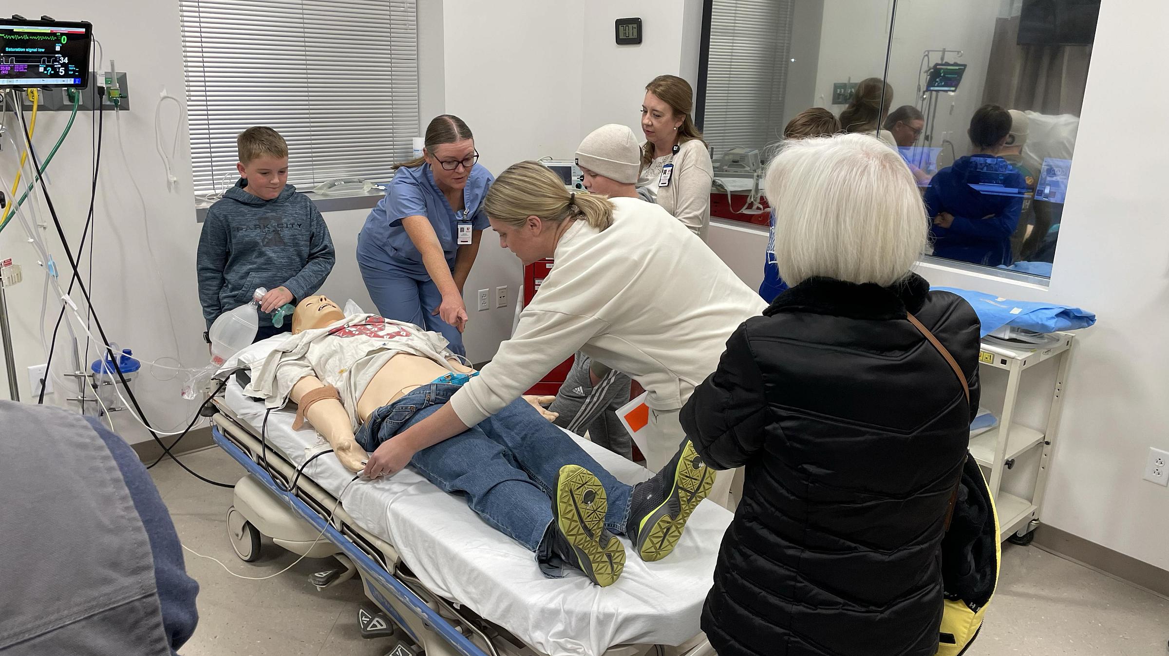 A family practices chest compressions and checking for pulse on a simulation center dummy under the guidance of a faculty member.