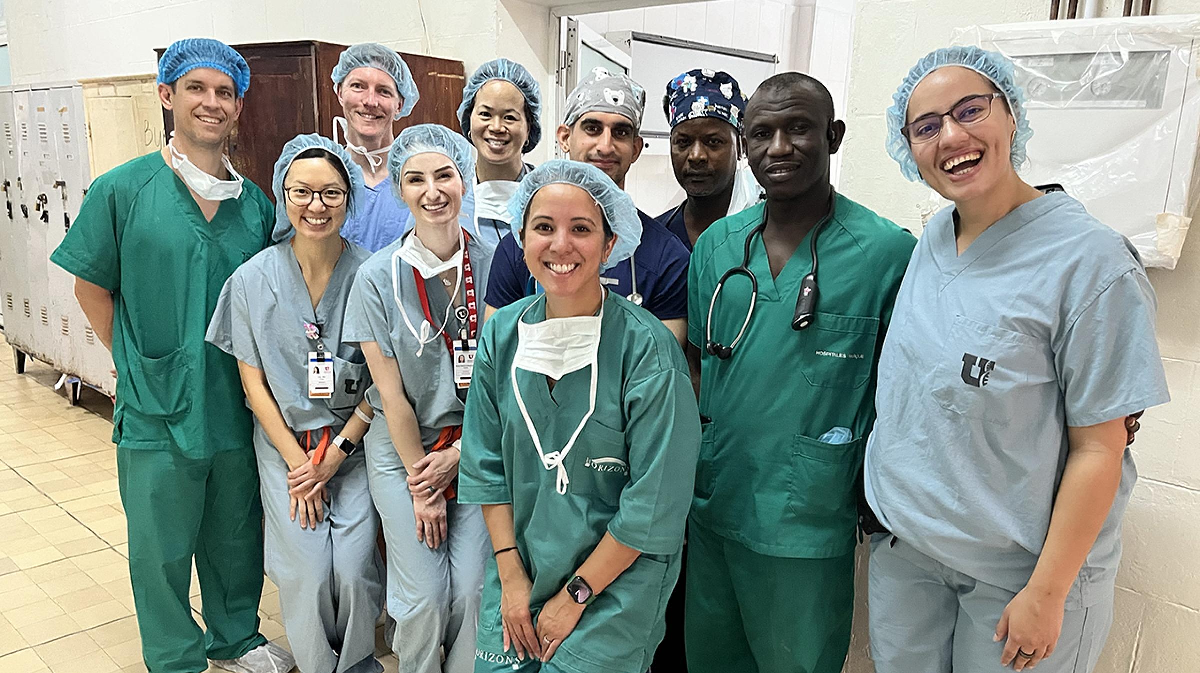 A group of 10 people in scrubs and caps smiling for a photo in a hallway in a medical facility.