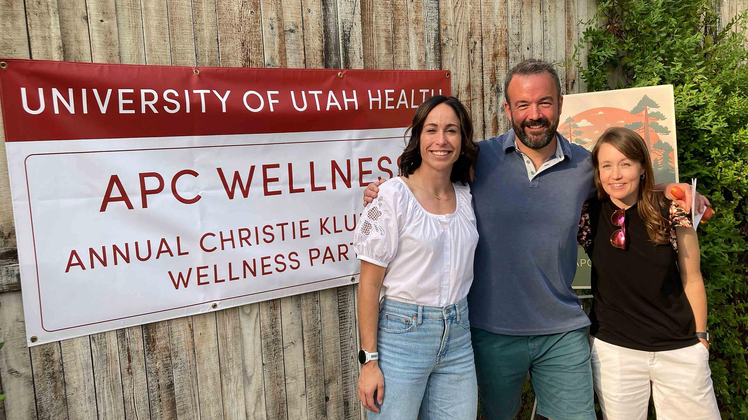 Dr. Orgain, and CRNA's Meg Schmidt, and Tori Taylor in front of the APC Wellness event sign.