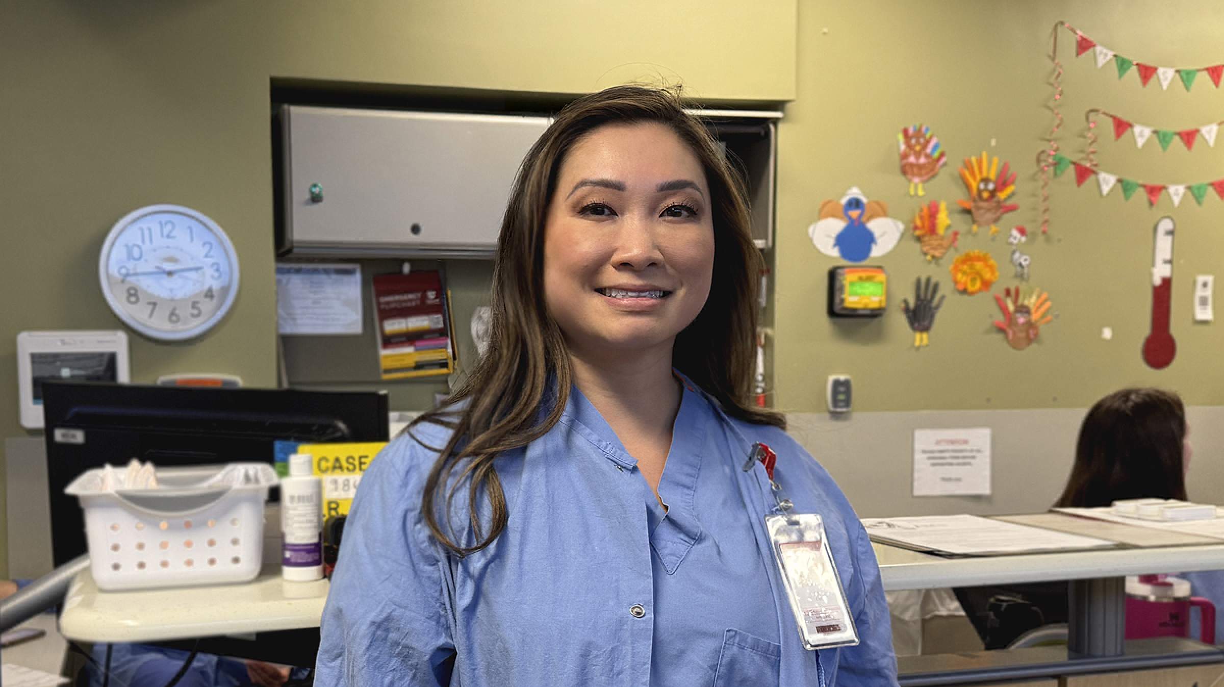 A CAA wearing blue scrubs standing in front of an OR desk smiling. 
