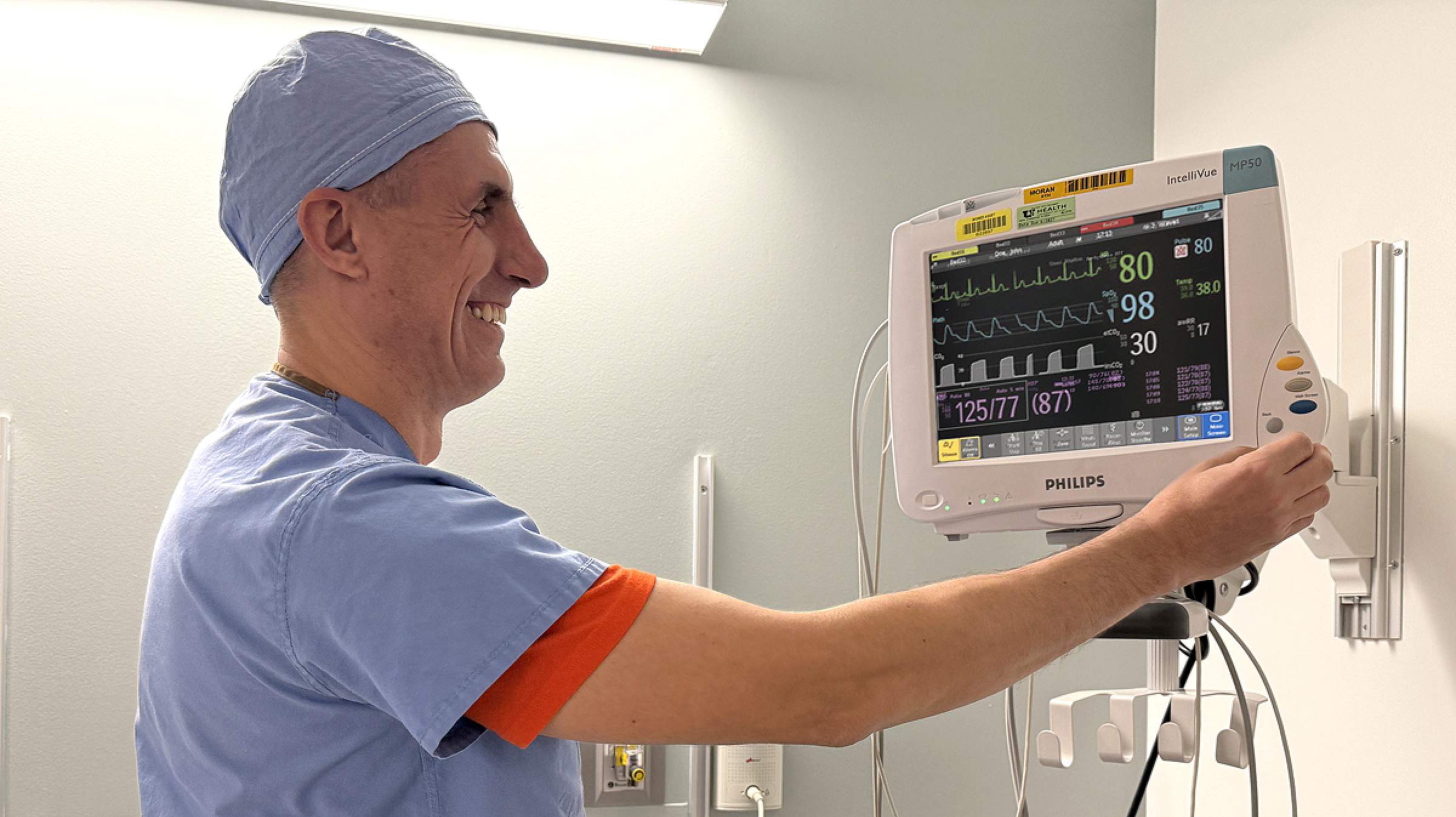 A CRNA wearing blue scrubs using a patient monitor in a room.