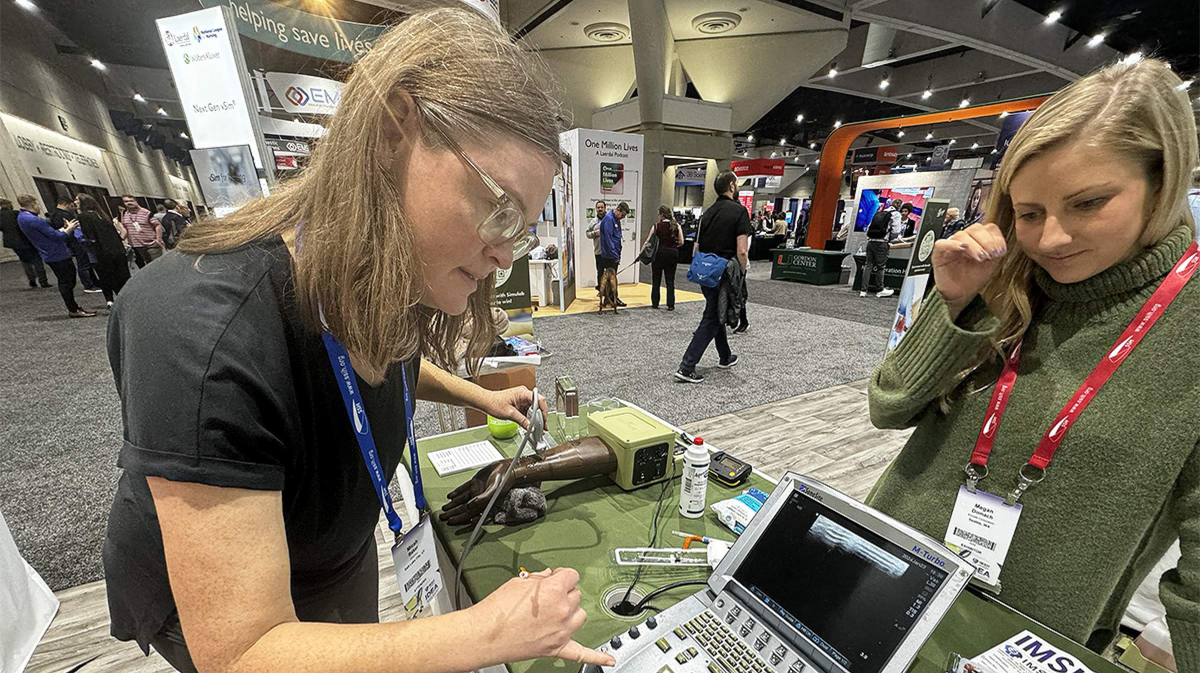 An instructor shows a conference attendee how to use a machine at their booth. 